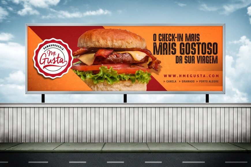 Outdoor da hamburgueria Me Gusta com fundo laranja e vermelho, exibindo um hambúrguer suculento com bacon, queijo, alface e tomate. Campanhas Offline.